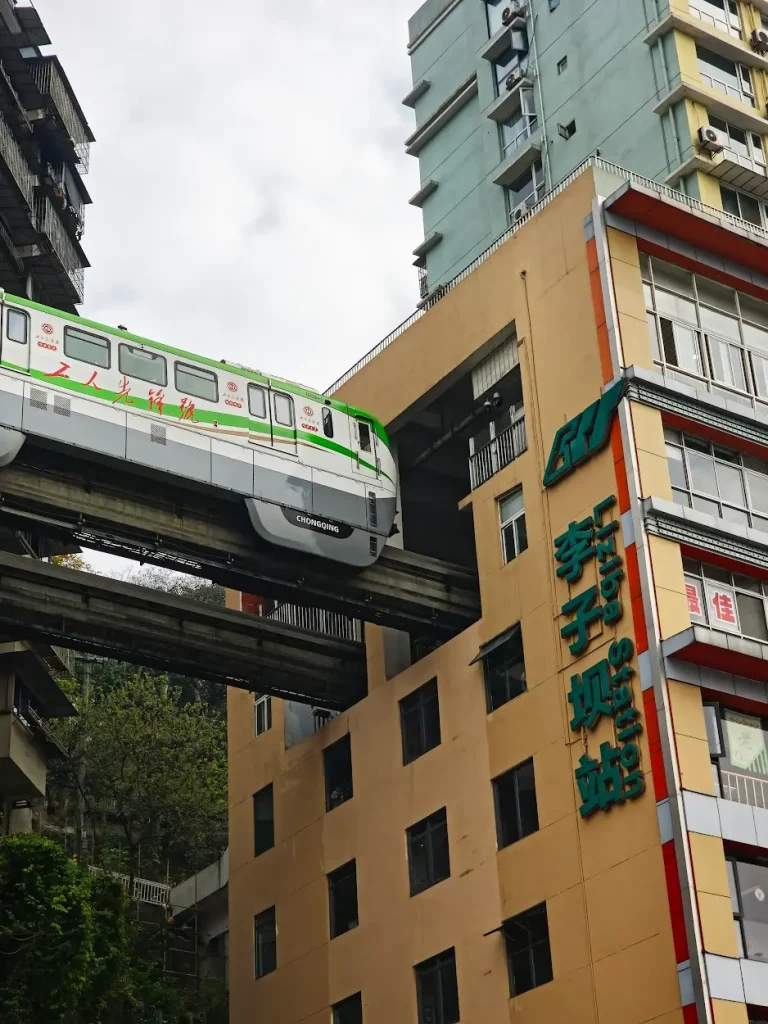 Monorail train passing through a building at Liziba Station in an urban area with surrounding high-rise structures.